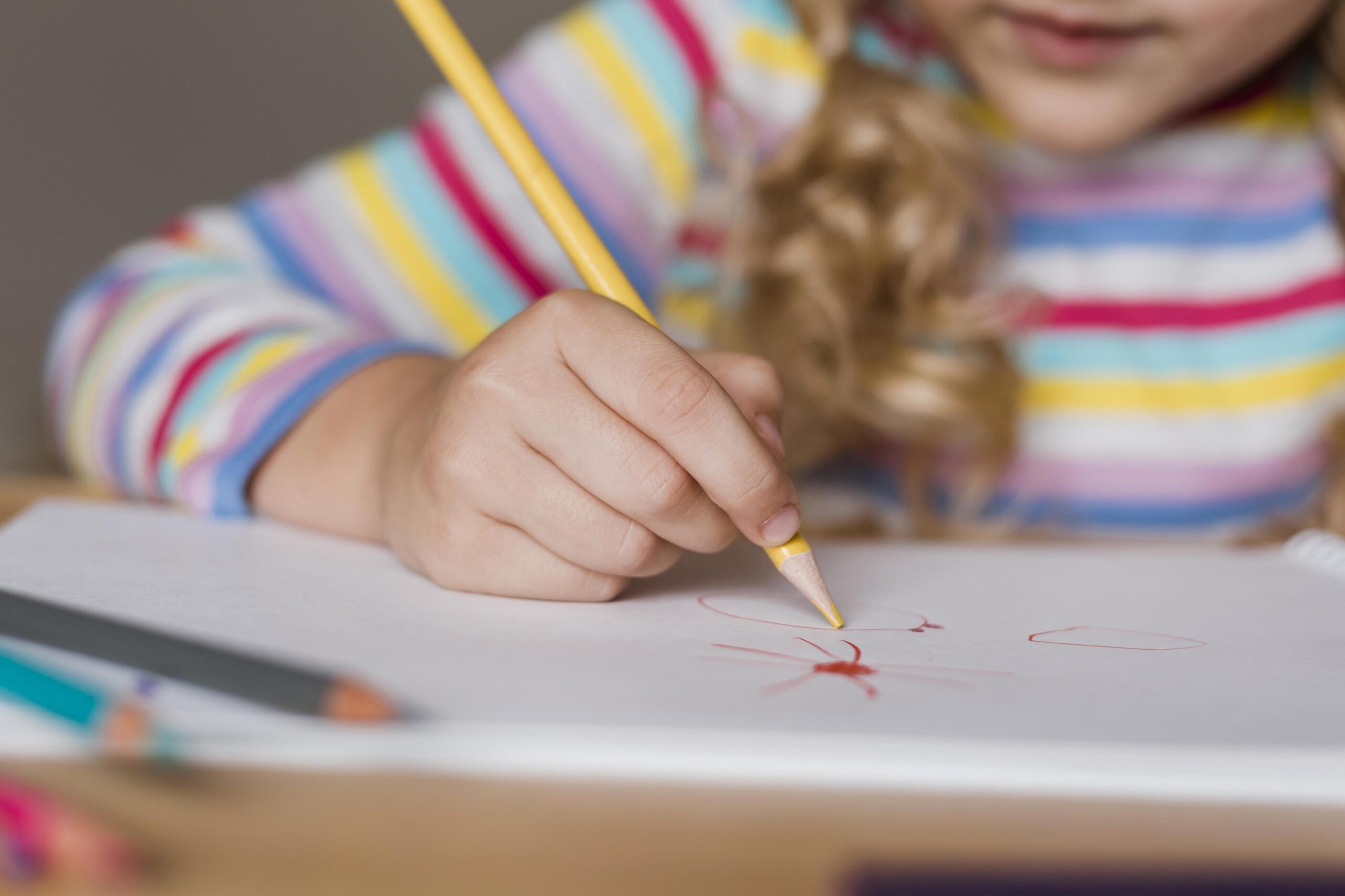 Kind tekent met kleurpotlood op papier.